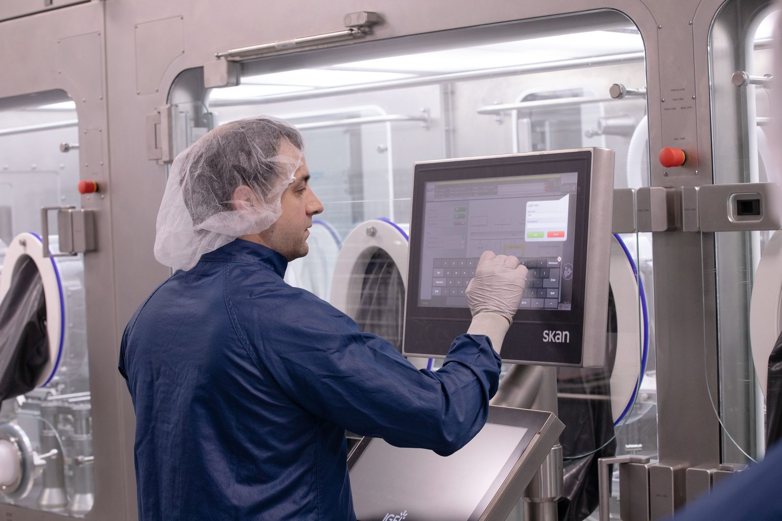 Technician operating isolator control panel during sterile injectable fill-finish manufacturing