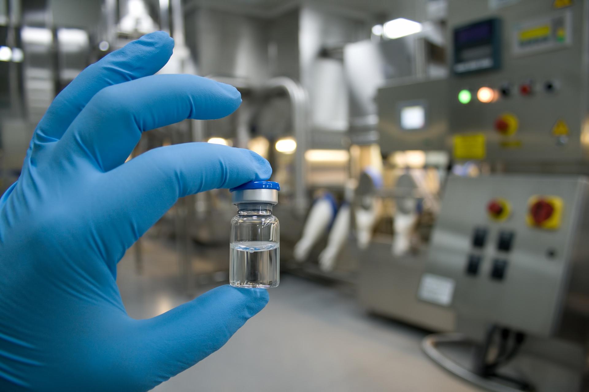 gloved hand holding filled vial in pharmaceutical manufacturing facility