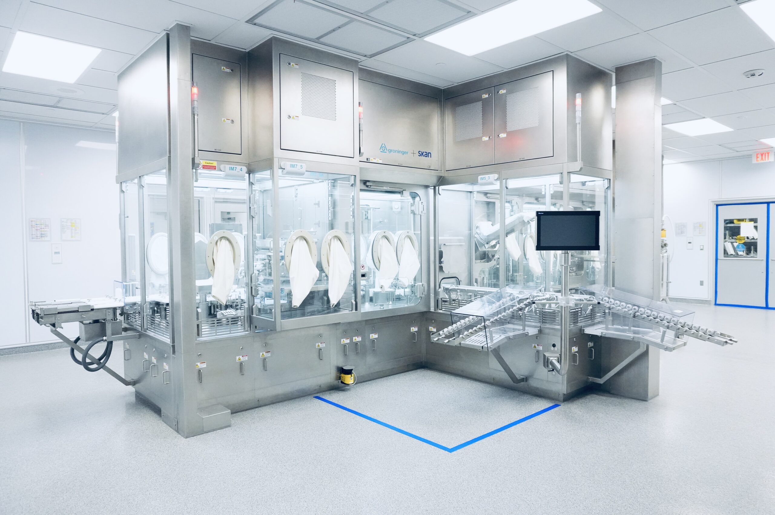 Front view of the Groninger + Skan sterile fill-finish isolator system with glove ports and integrated vial conveyor in a cleanroom.