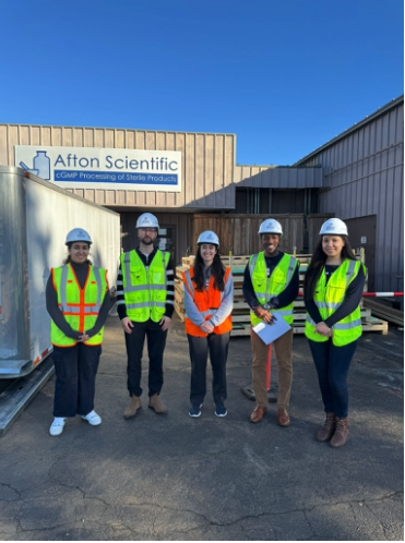 Five people wearing high-visibility vests and hard hats stand outside an Afton Scientific cGMP processing facility.