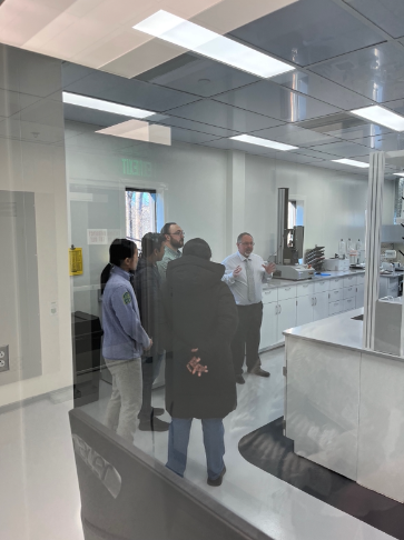 Small group listens to a presenter inside a clean, glass-walled laboratory space.
