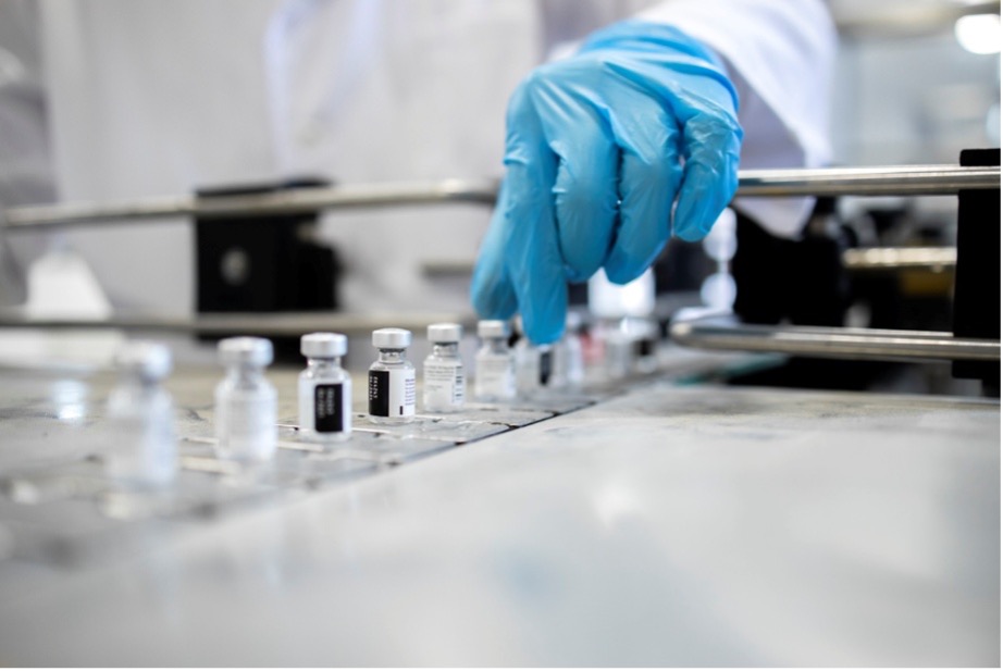 Modern sterile fill-finish cleanroom with automated vial filling line and operators in aseptic gowns under unidirectional airflow. ​