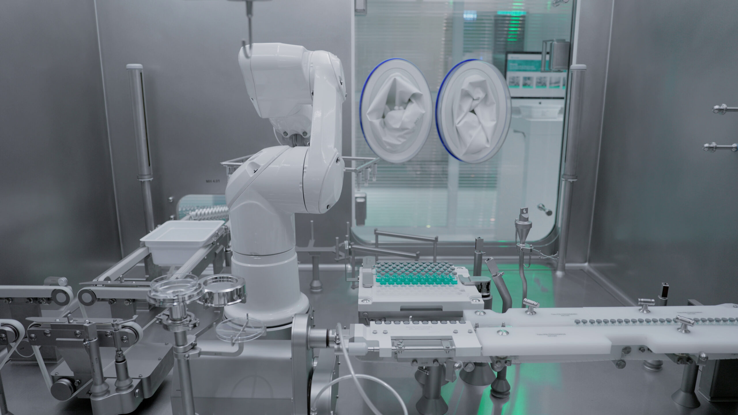 Robotic aseptic filling line operating inside a stainless steel isolator, loading trays of sterile injectable vials in a pharmaceutical cleanroom.