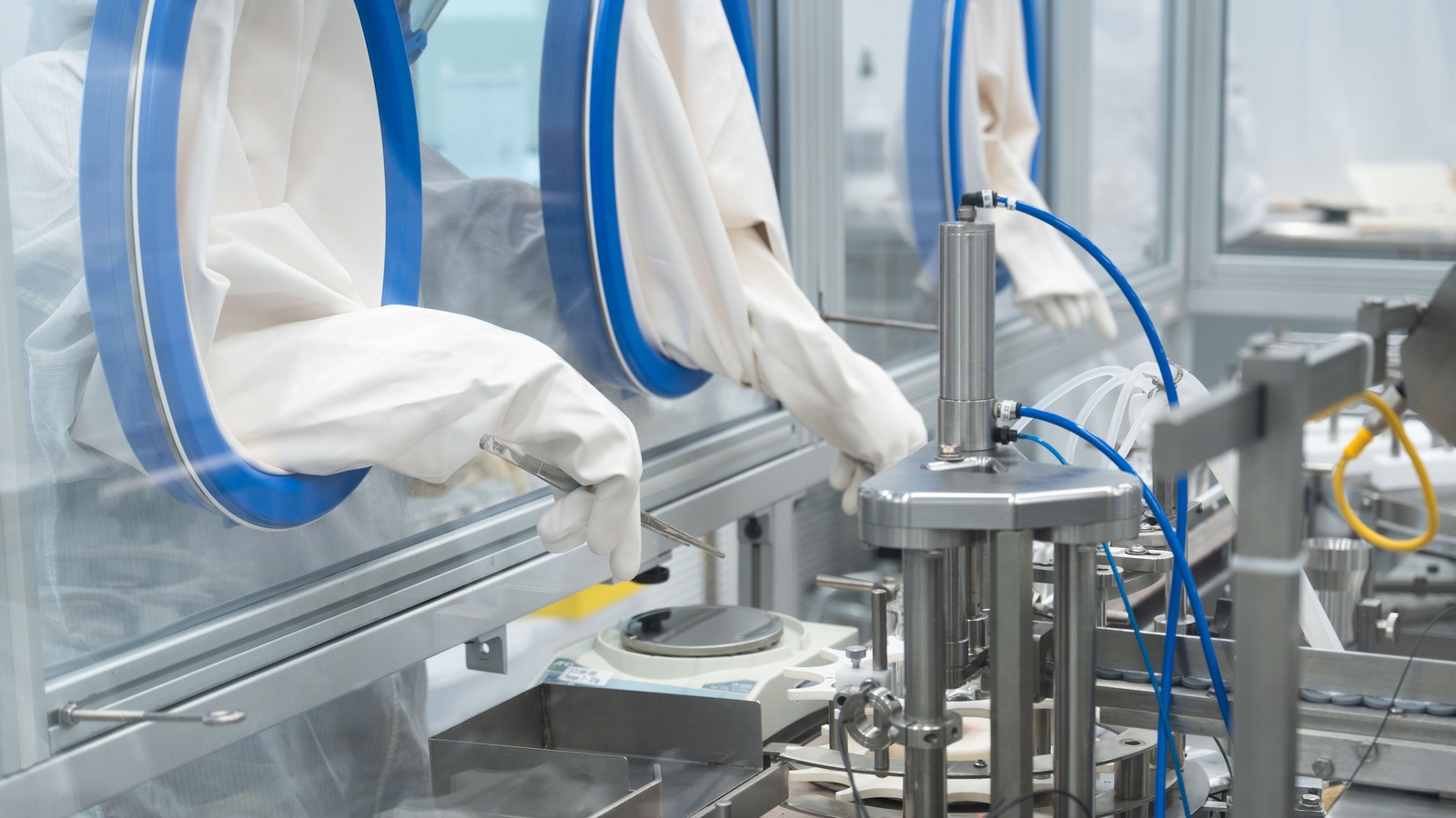 Gloved hands using tweezers inside a sterile isolator during aseptic fill-finish manufacturing