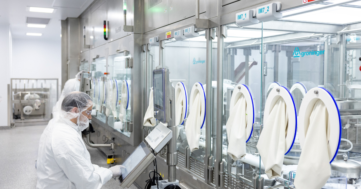 Gowned operator monitoring a sterile injectable isolator filling line in a cleanroom